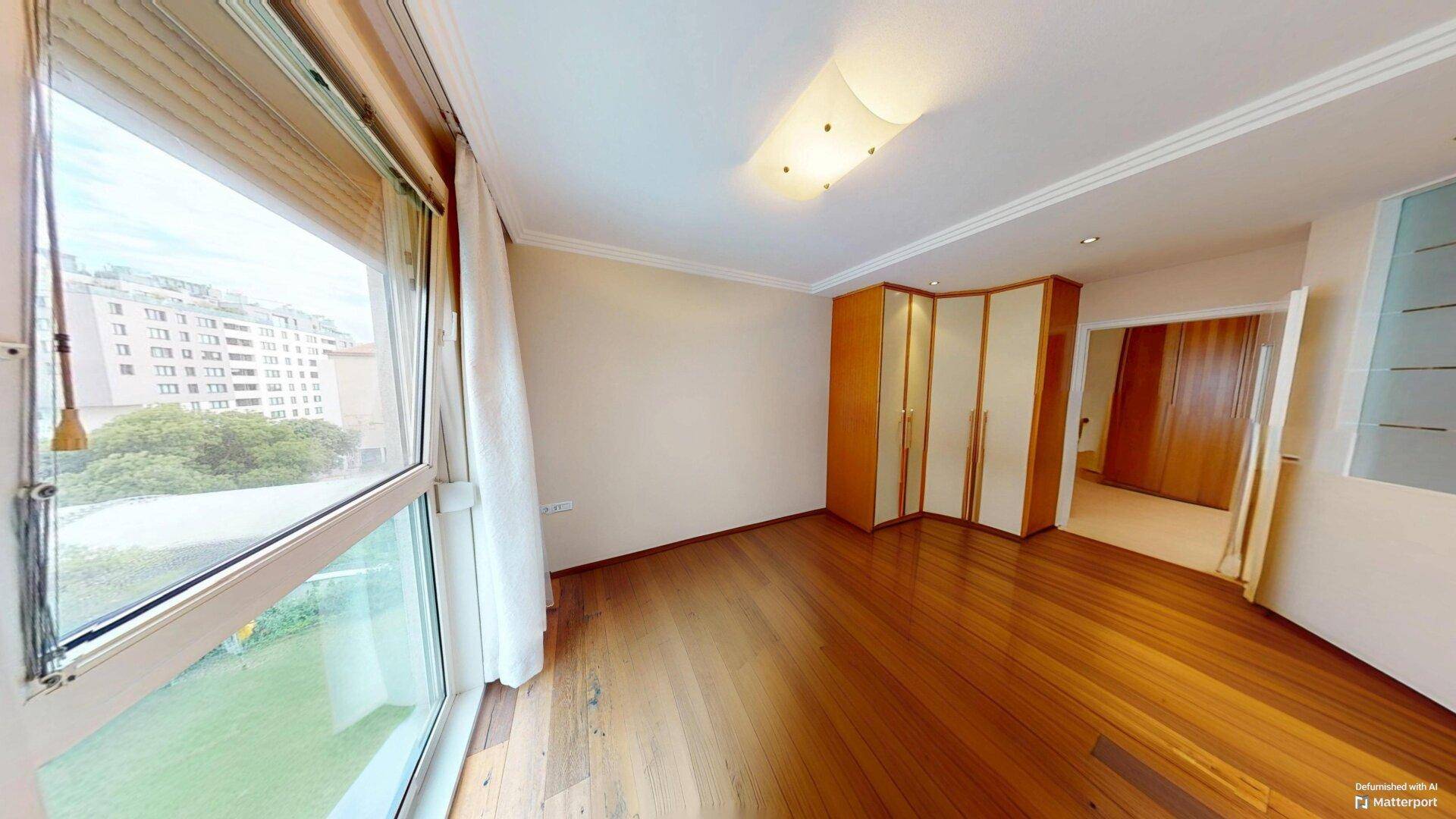 Geräumiges Schlafzimmer mit Parkettboden, Einbauschränken und großem Fenster mit Blick ins Grüne.