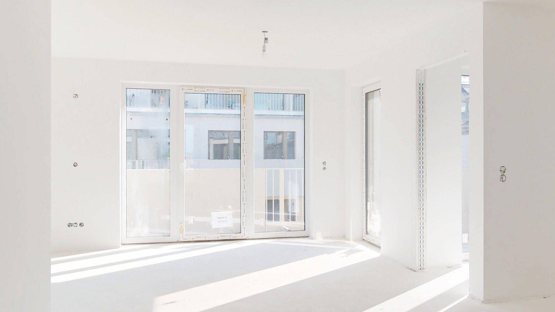 Heller, unmöblierter Wohnraum mit großen Fenstern und vorbereiteten Elektroinstallationen.
