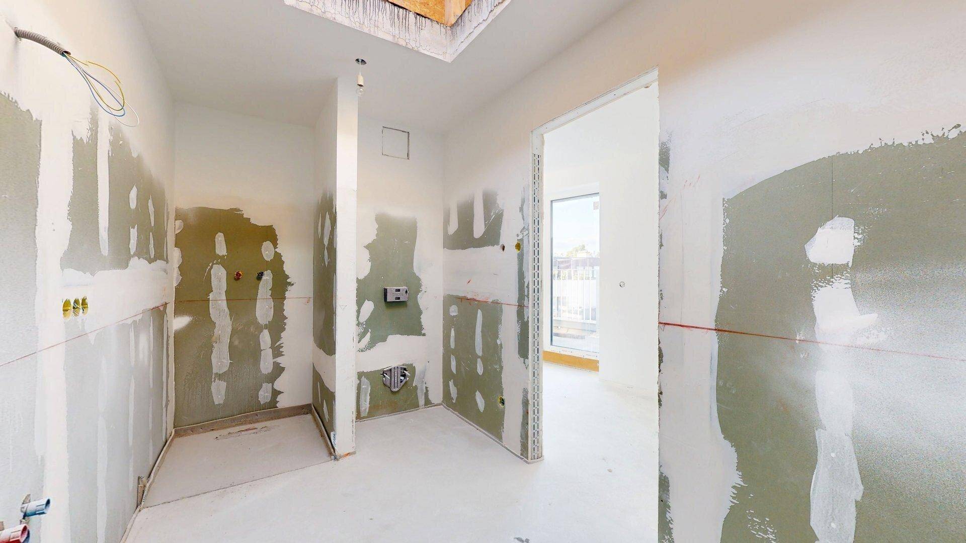 Badezimmer im Rohbau mit vorbereiteten Installationen und Zugang zu einem Außenbereich.