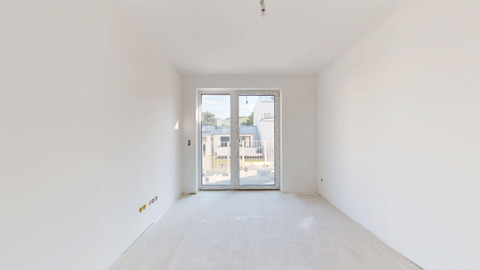 Heller, unmöblierter Raum im Rohbau mit einer großen Fensterfront und Blick ins Grüne.