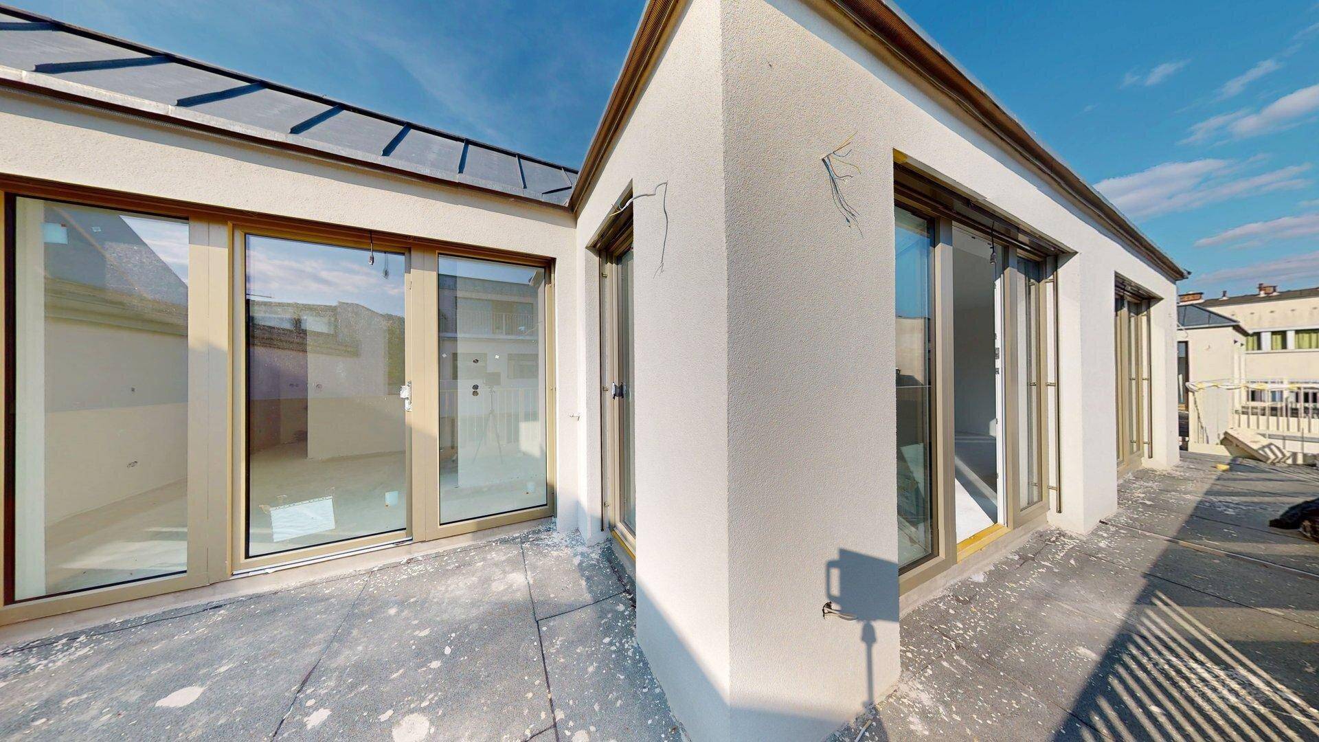 Eckbereich eines Gebäudes mit großen Schiebetüren, die zu einer unfertigen Dachterrasse führen.