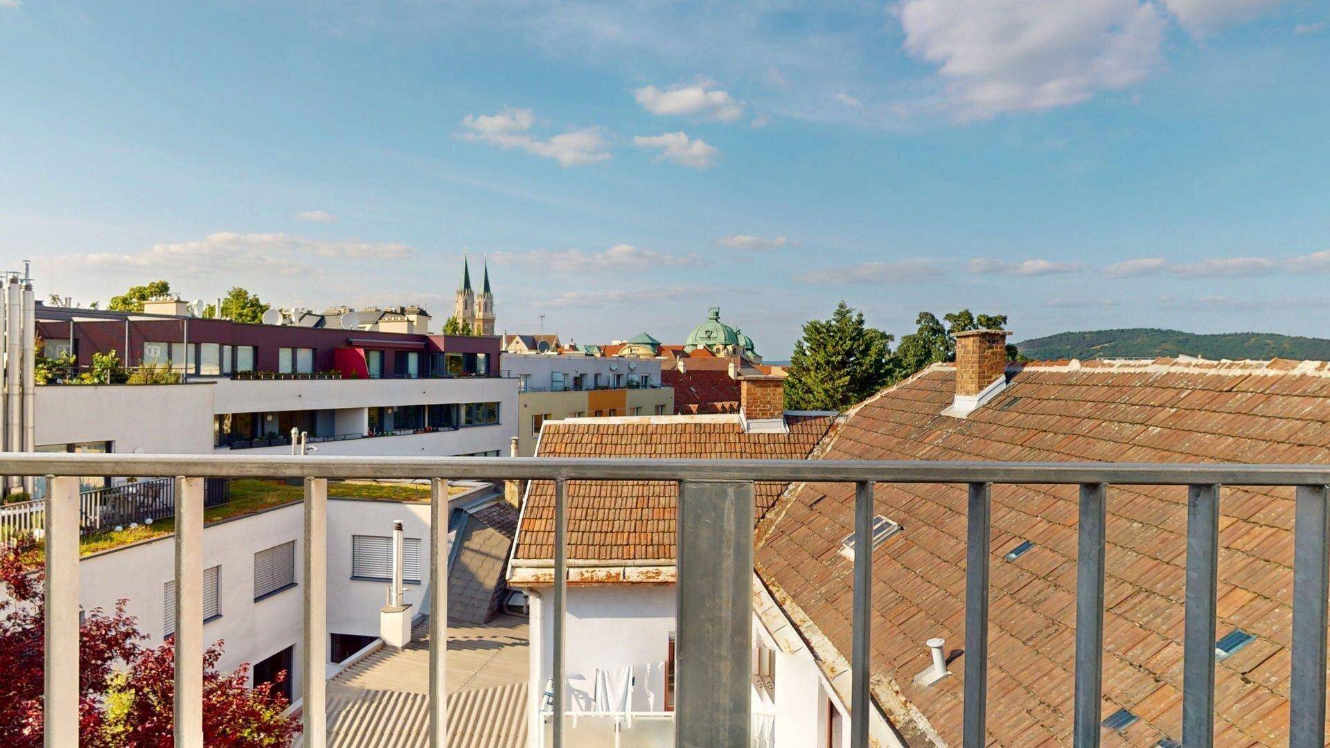 Panoramablick von einem Balkon über Dächer und die Stadt mit einem historischen Kirchturm.