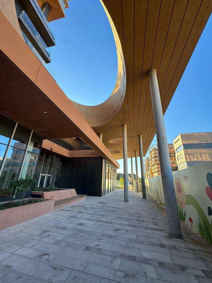 Moderne Architektur mit geschwungener Holzverkleidung und großen Glasflächen an einem sonnigen Tag.