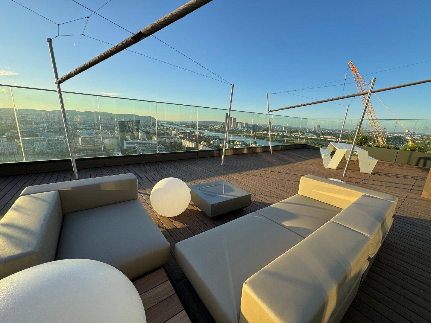 Geräumige Dachterrasse mit modernen Loungemöbeln und weitem Blick über die Stadt bei Sonnenuntergang.