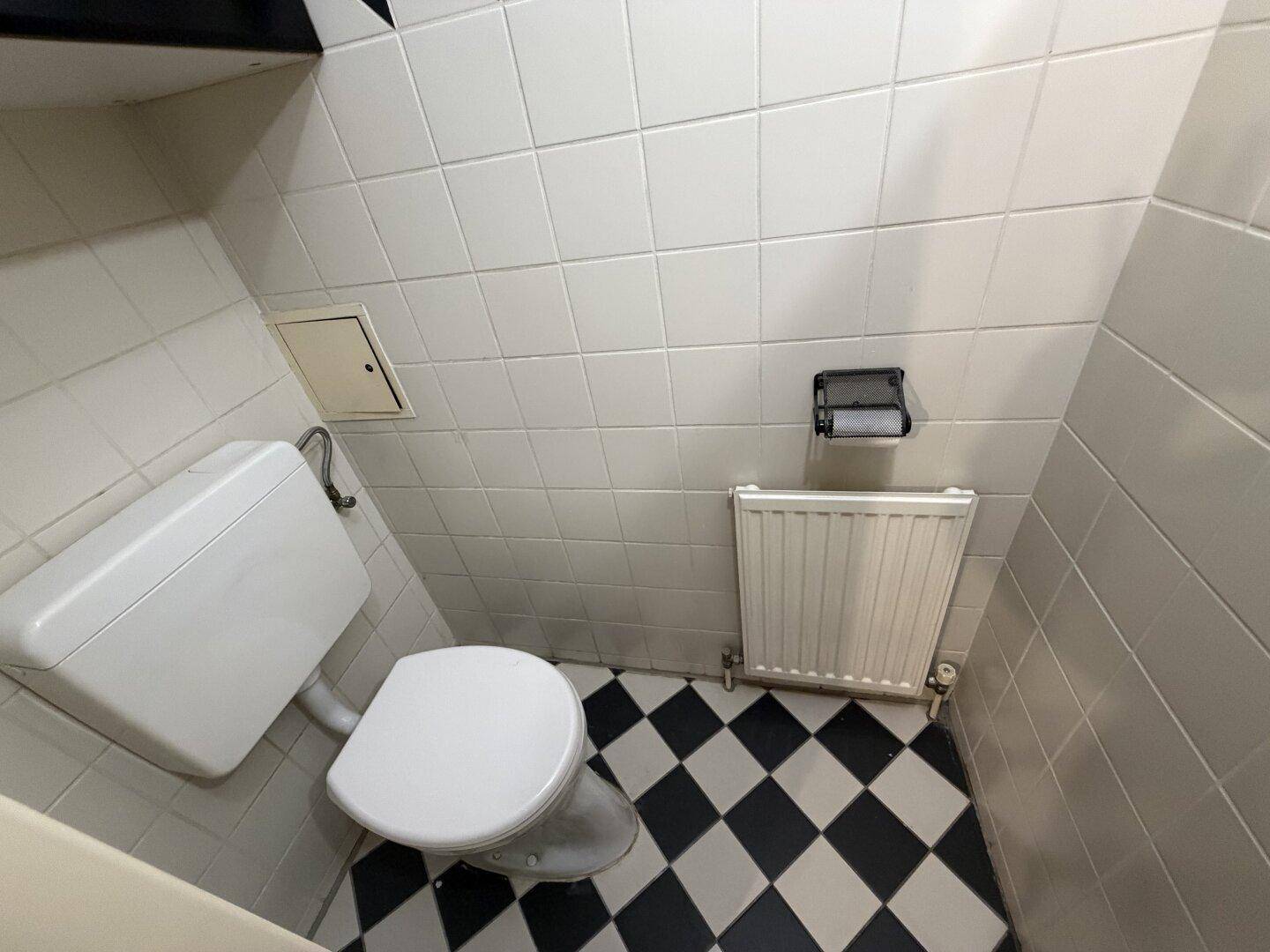 Separates WC mit Toilette, Heizkörper und auffälligem schwarz-weiß kariertem Fliesenboden.