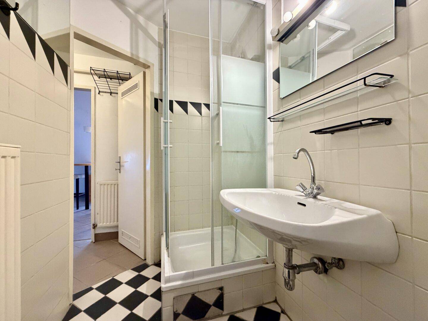 Funktionales Badezimmer mit Duschkabine, Waschbecken und charakteristischem Schachbrettmuster-Boden.