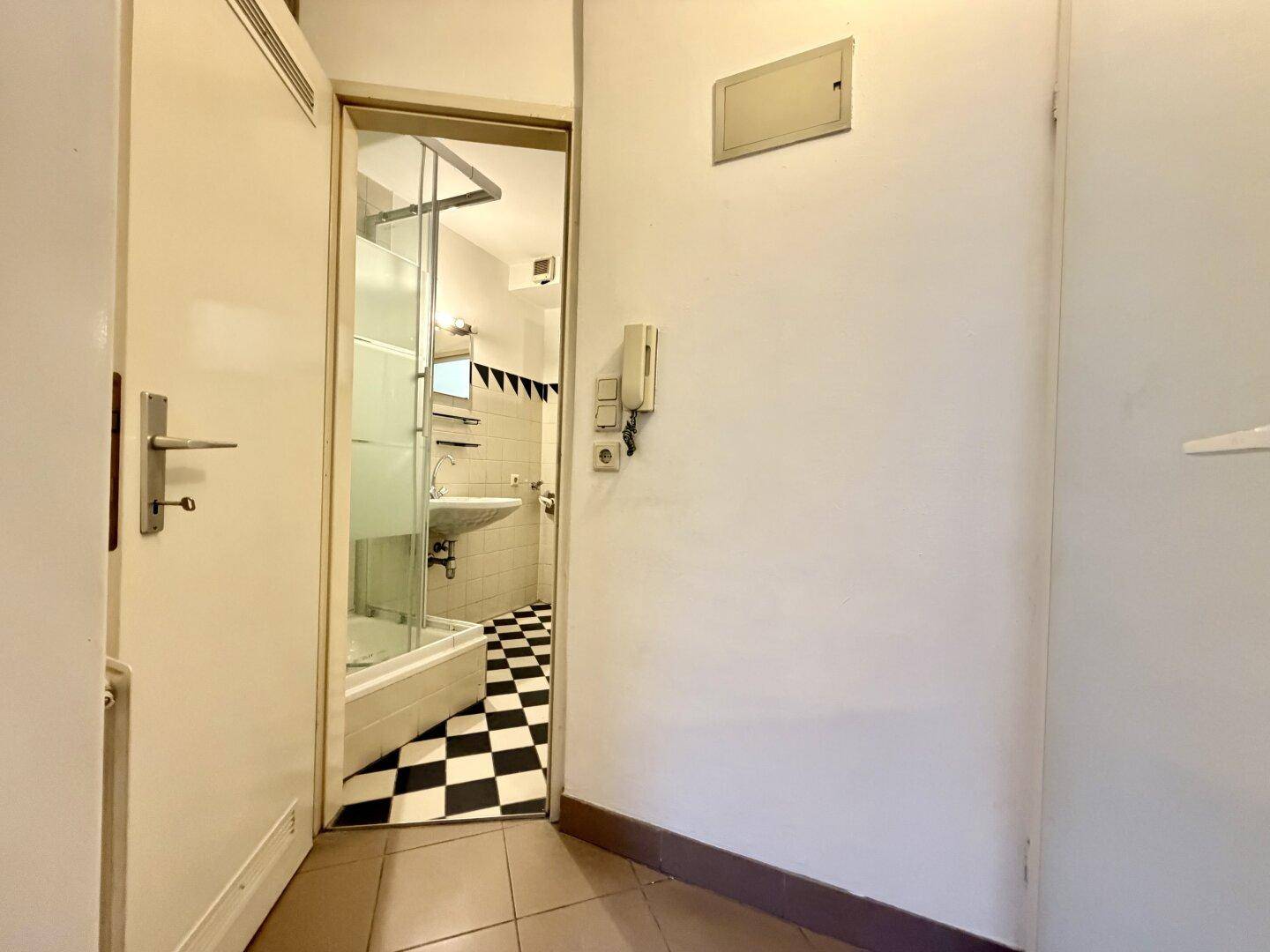 Schmaler Flur mit Zugang zu einem Badezimmer, gekennzeichnet durch schwarz-weiß karierten Boden.