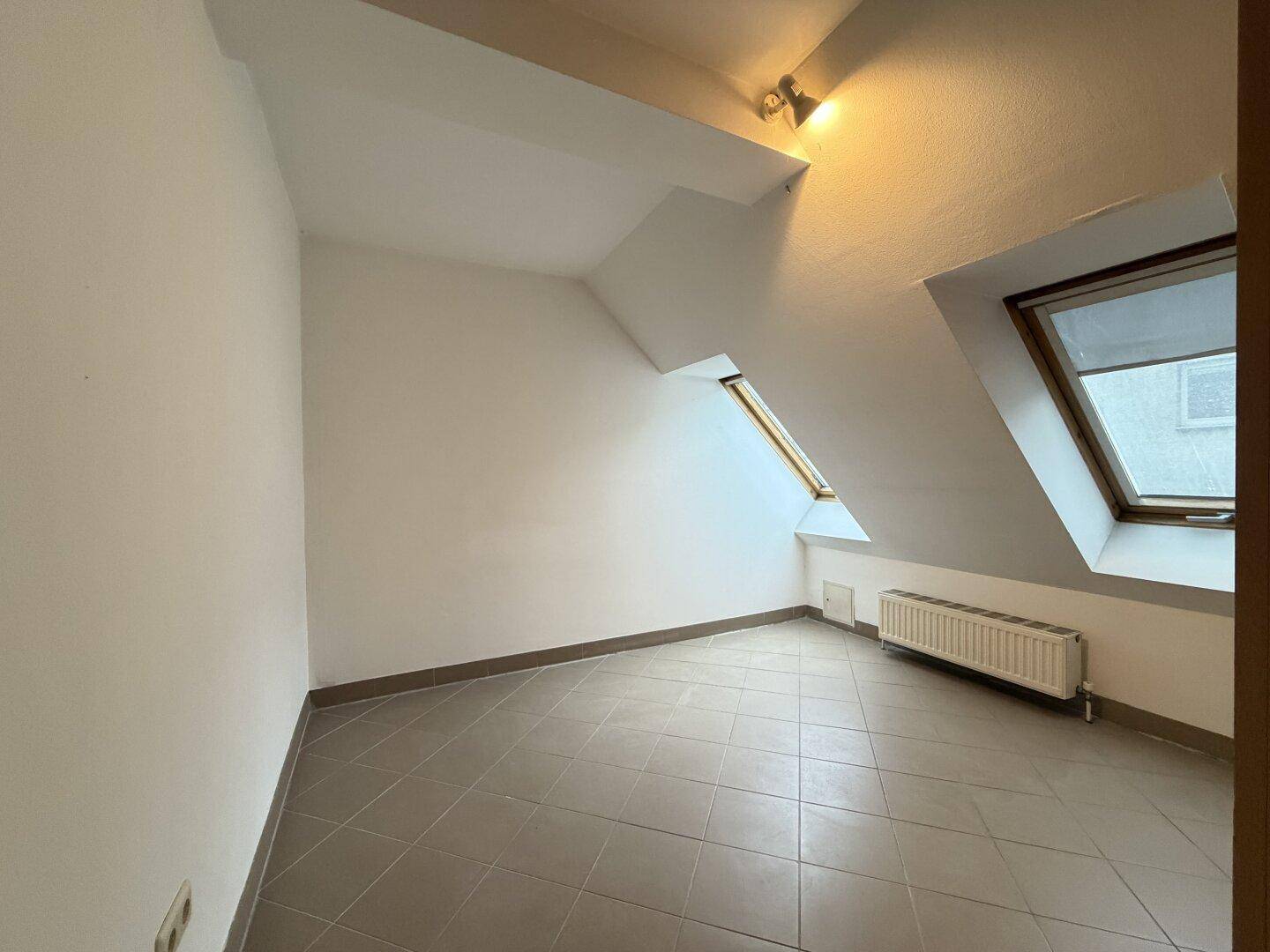 Gemütliches Zimmer im Dachgeschoss mit schrägen Wänden, Dachfenster und Heizkörper.
