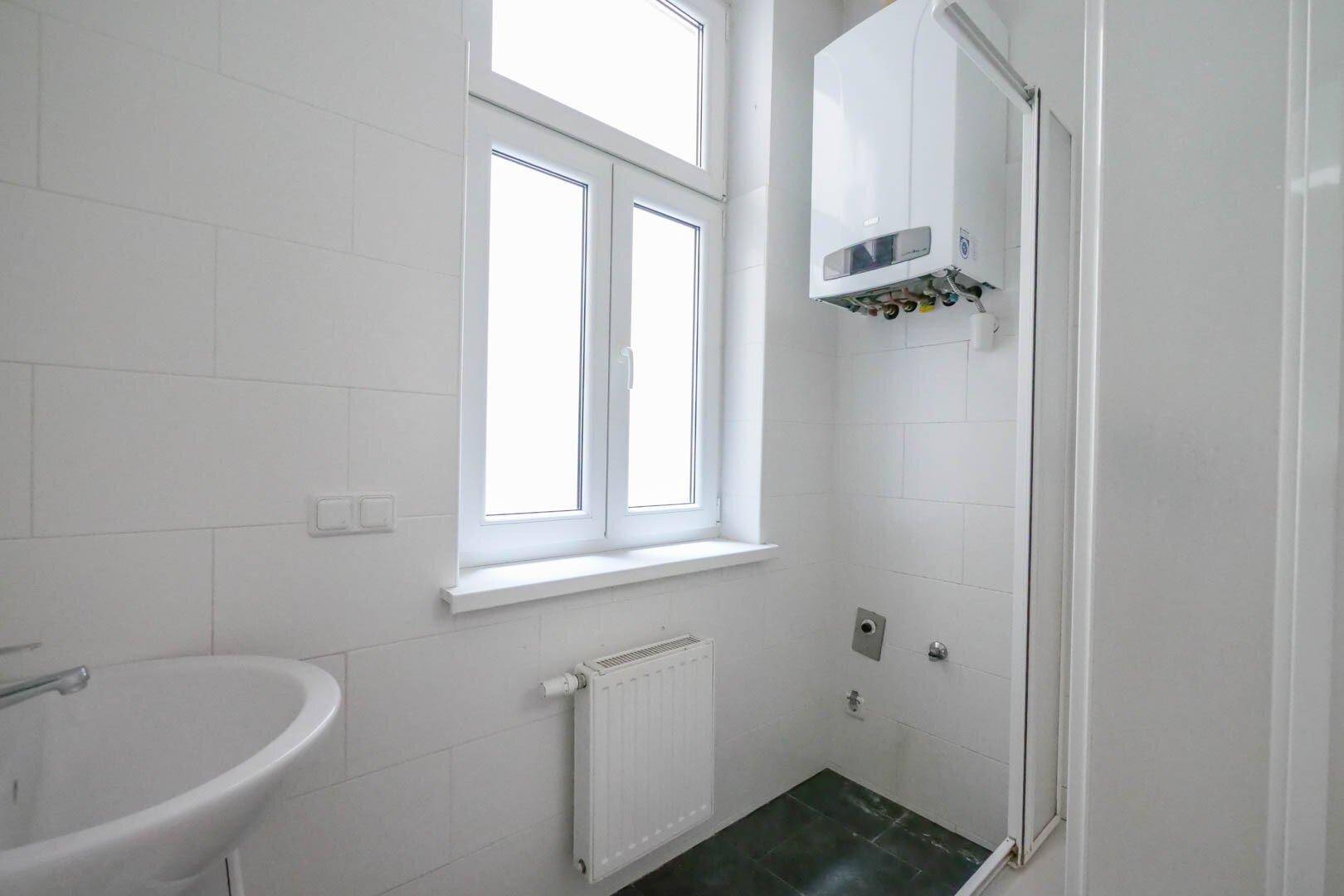 Modern gefliestes Badezimmer mit Fenster, Waschbecken und Duschbereich mit Gastherme.