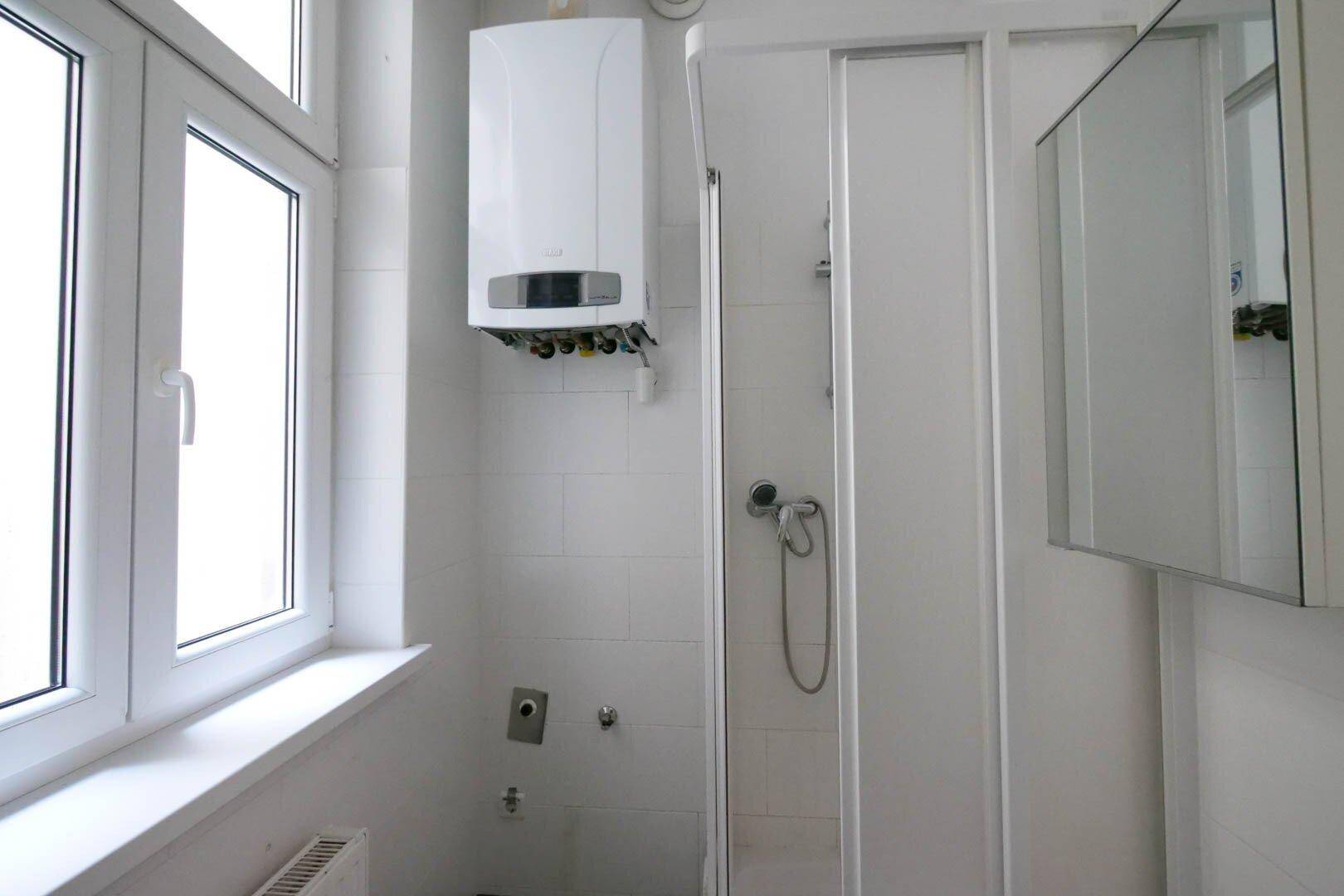 Duschbereich im Badezimmer mit Gastherme, Duschkabine und Spiegelschrank.