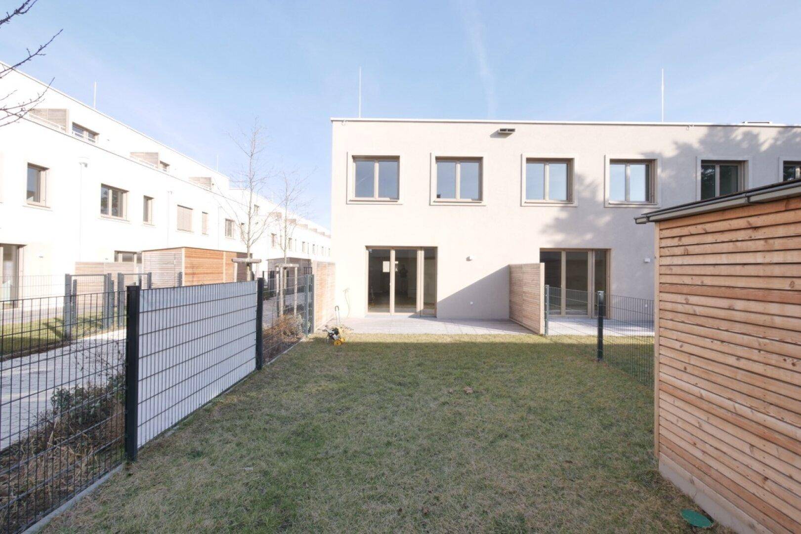 Rückansicht eines modernen Reihenhauses mit Garten und Gartenhaus.