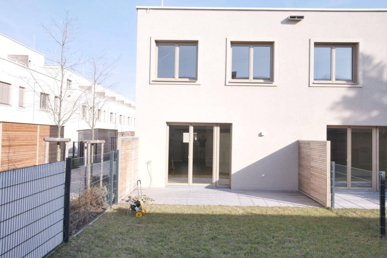 Rückseite eines Reihenhauses mit gepflasterter Terrasse und Rasenfläche.