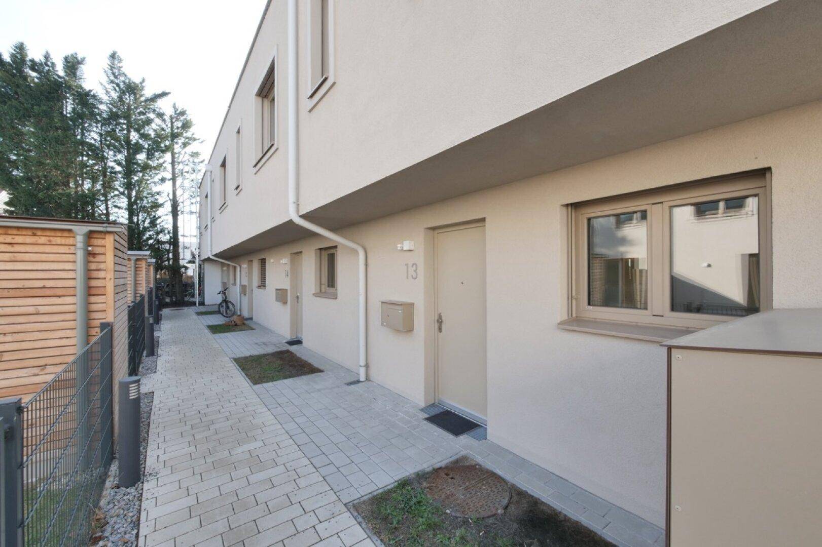 Eingangsbereich moderner Reihenhäuser mit gepflastertem Zugang und Hausnummern.
