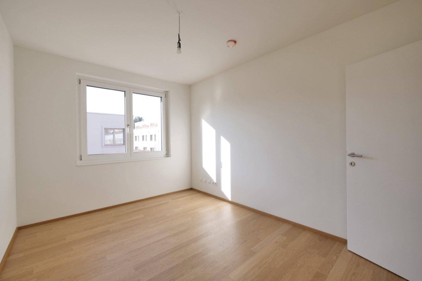 Helles Schlafzimmer mit Parkettboden und Fenster, bereit zur Einrichtung.