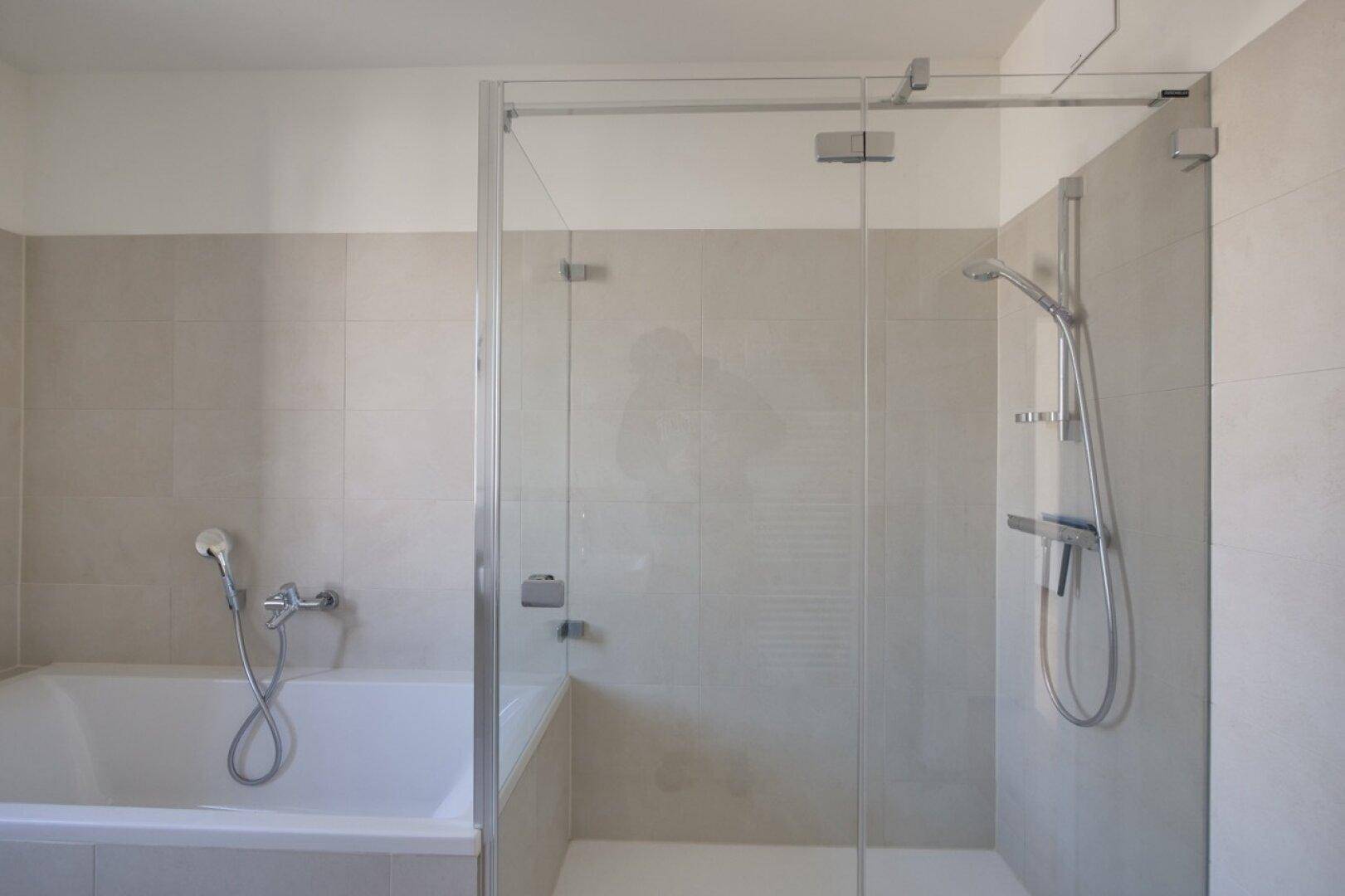 Duschbereich mit Glasabtrennung und Badewanne in einem modernen Badezimmer.
