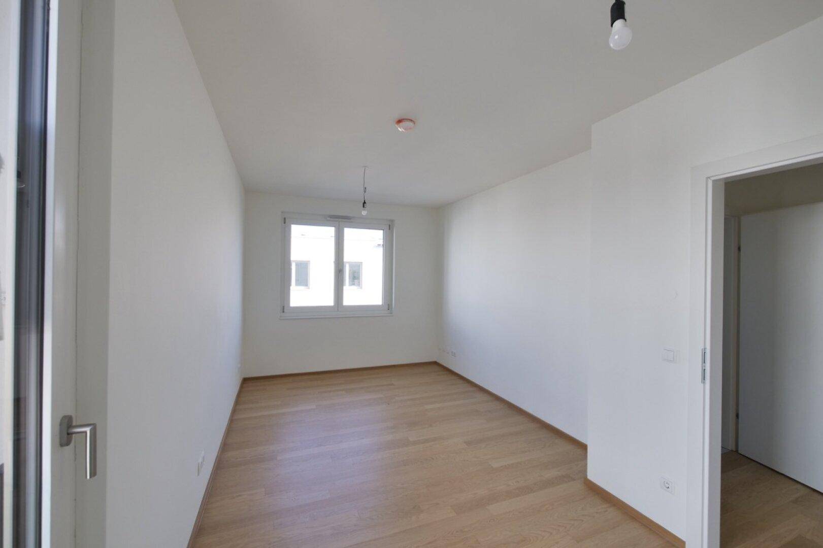 Helles Zimmer mit Parkettboden und Fenster, bietet viel Tageslicht.