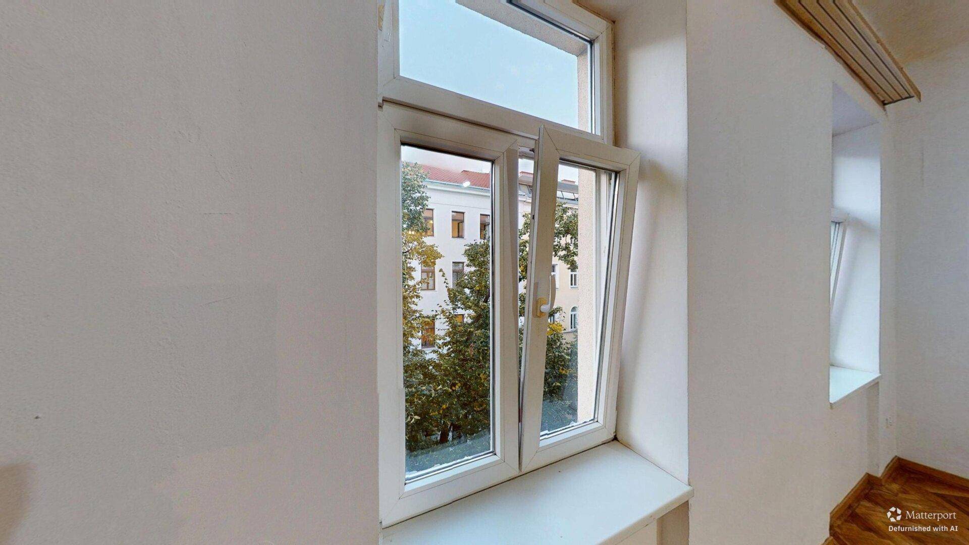 Fenster mit Blick auf Bäume und umliegende Gebäude, das viel Tageslicht spendet.