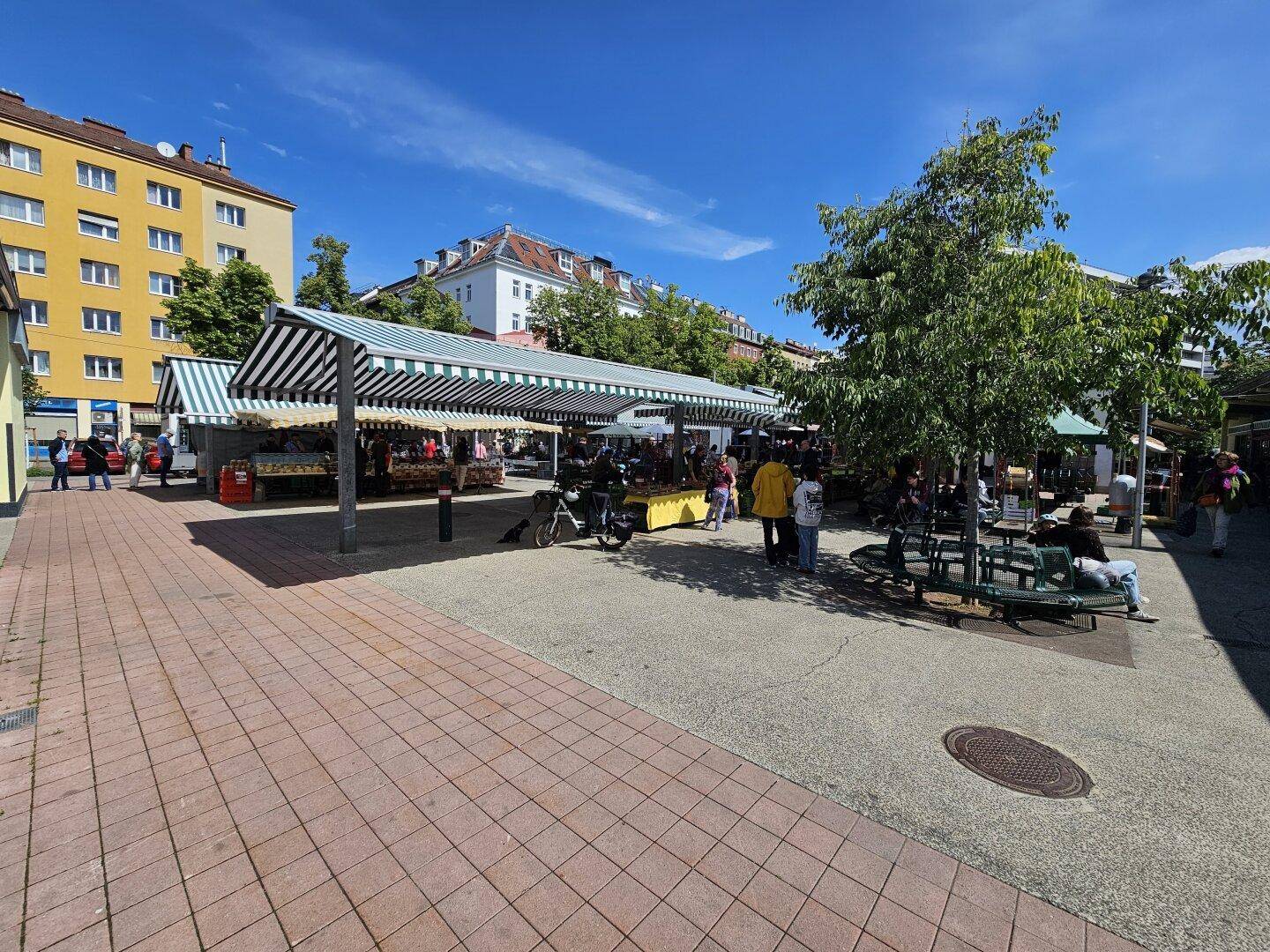 Lebhafter Wochenmarkt unter gestreiften Markisen an einem sonnigen Tag.