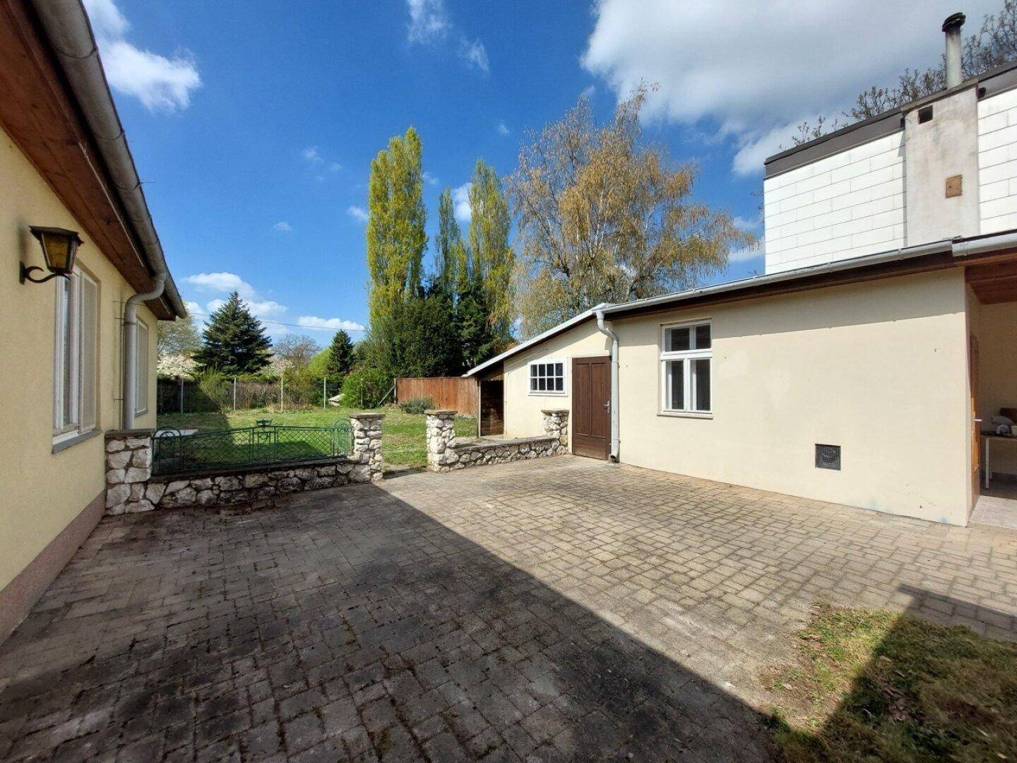 Gepflasterter Hofbereich neben dem Gebäude mit Zugang zum grünen Garten.