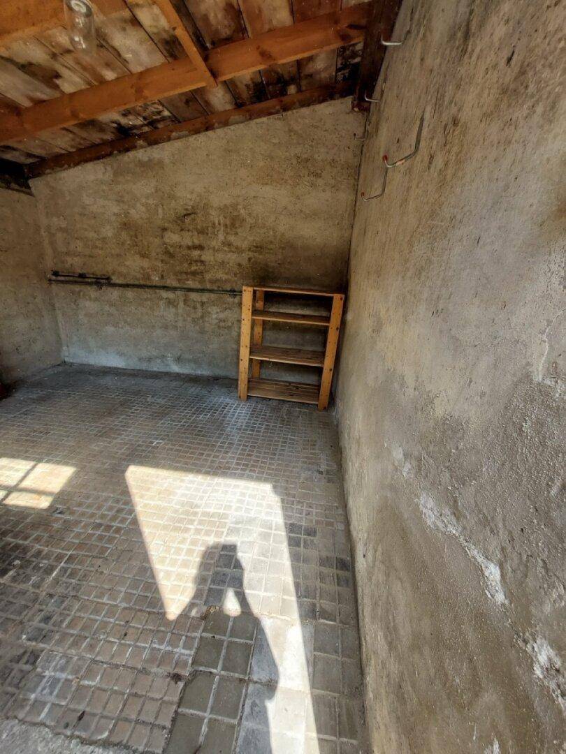 Kleiner Abstellraum mit Betonwänden und Fliesenboden, praktisch für zusätzliche Lagerung.