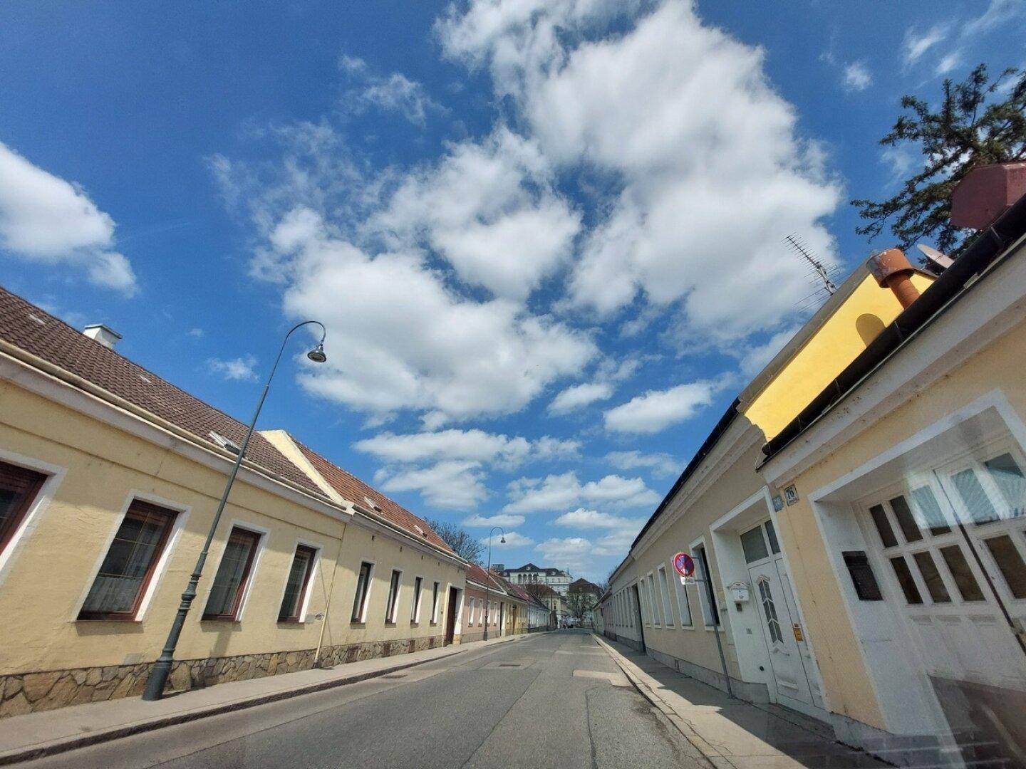 Blick die Straße hinunter mit gelben Altbauten, Ziegeldächern und einem weiten blauen Himmel.