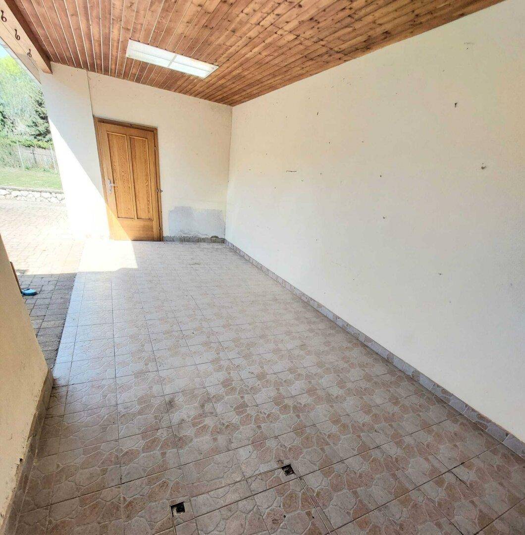 Überdachte Veranda mit Fliesenboden und Holzdecke, bietet Schutz und Gemütlichkeit.