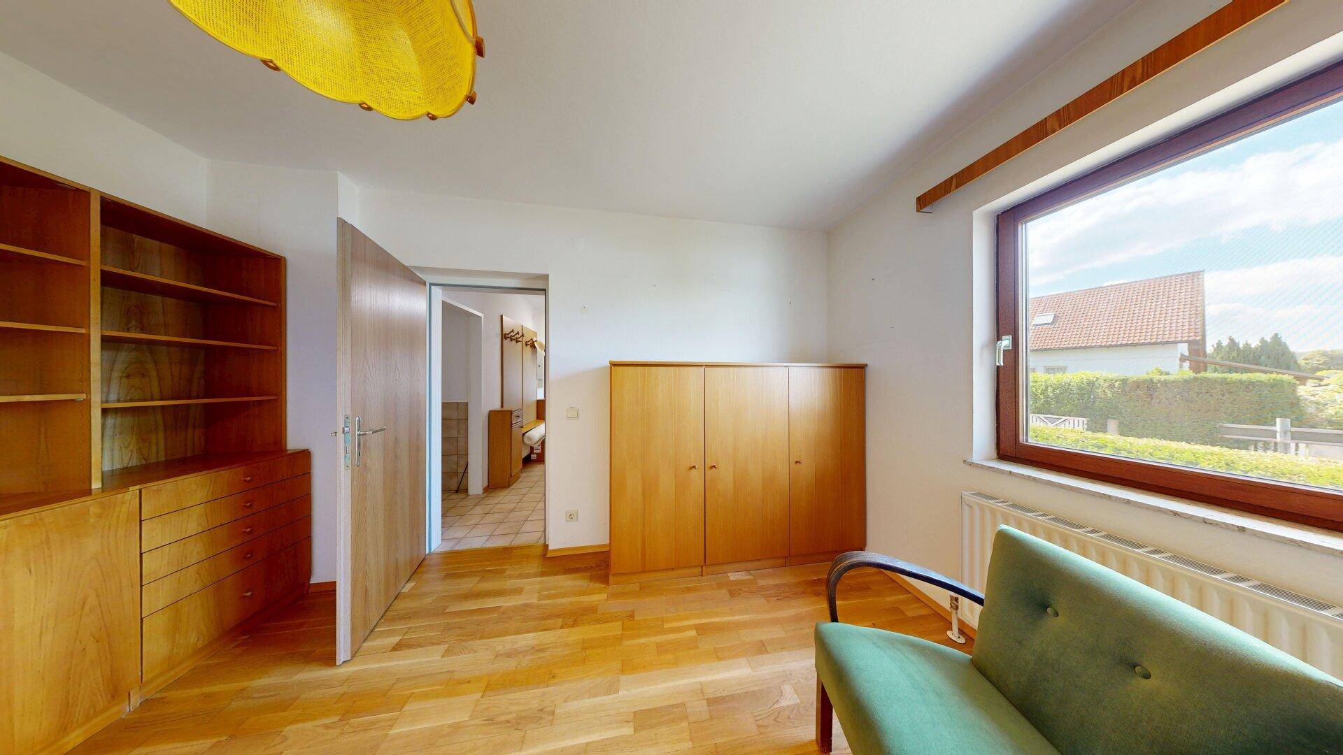 Helles Schlafzimmer mit Parkettboden, Einbauschränken und großem Fenster mit Blick ins Grüne.