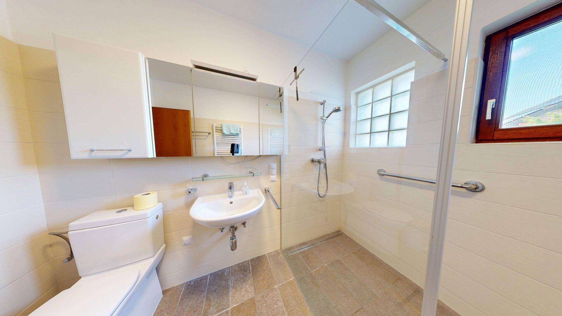 Modernes Badezimmer mit ebenerdiger Dusche, WC, Waschbecken und Haltegriffen für Barrierefreiheit.