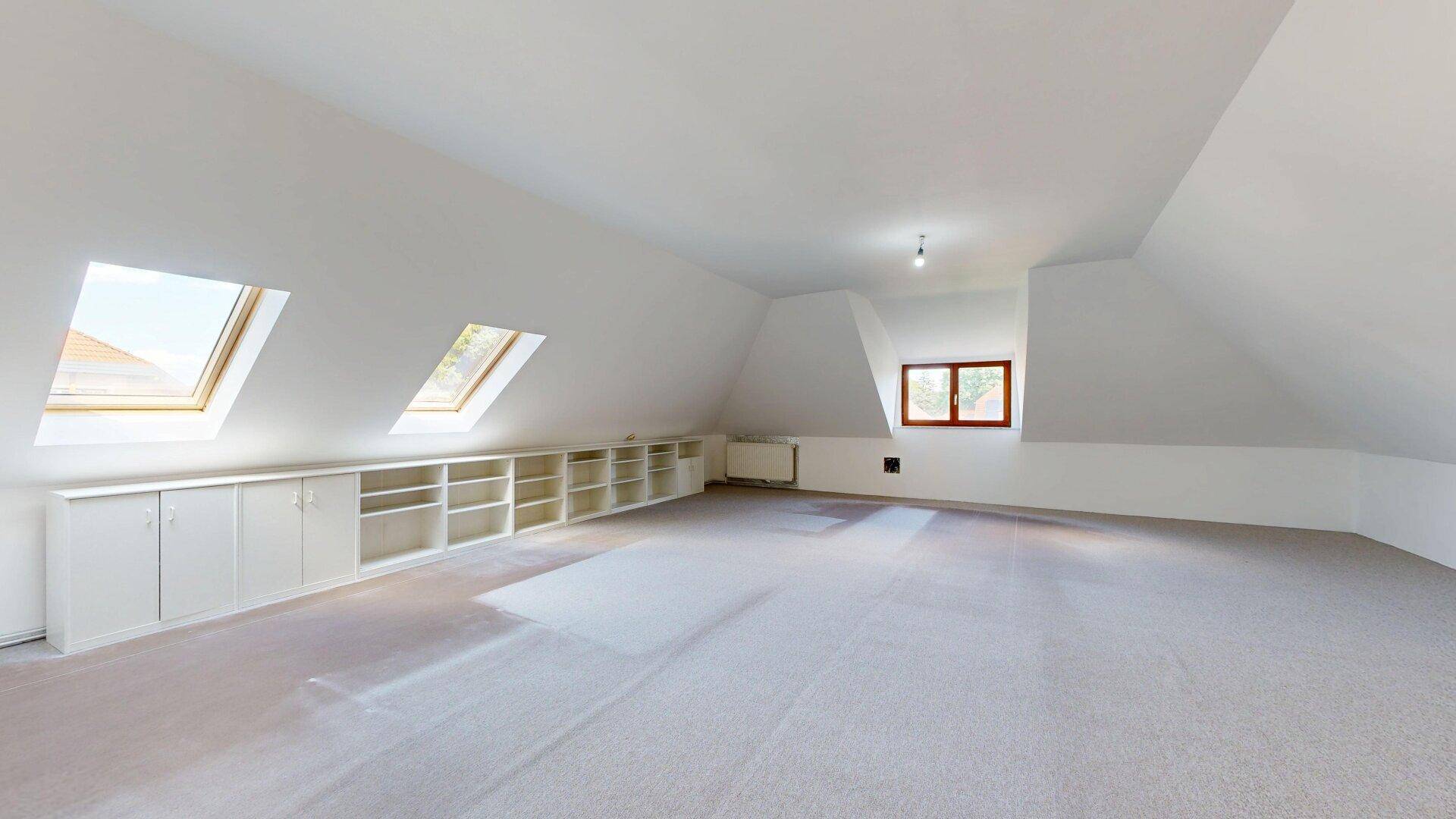 Geräumiges Dachzimmer mit Dachschrägen, Einbauregalen und hellen Dachfenstern.