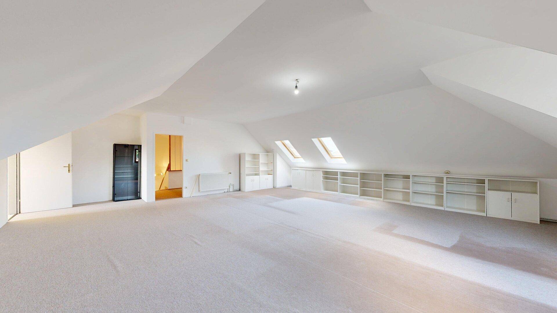 Weitläufiges Dachzimmer mit Teppichboden, Dachschrägen und integrierten Regalsystemen.