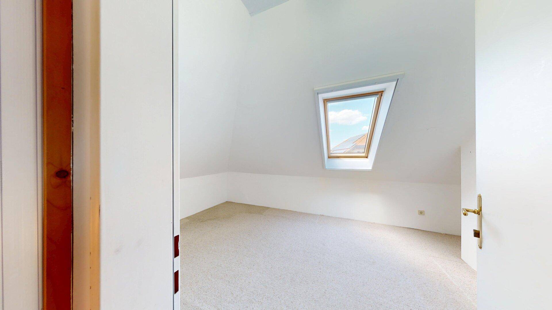 Kleines Dachzimmer mit Teppichboden und einem Dachfenster, ideal als Kinder- oder Gästezimmer.