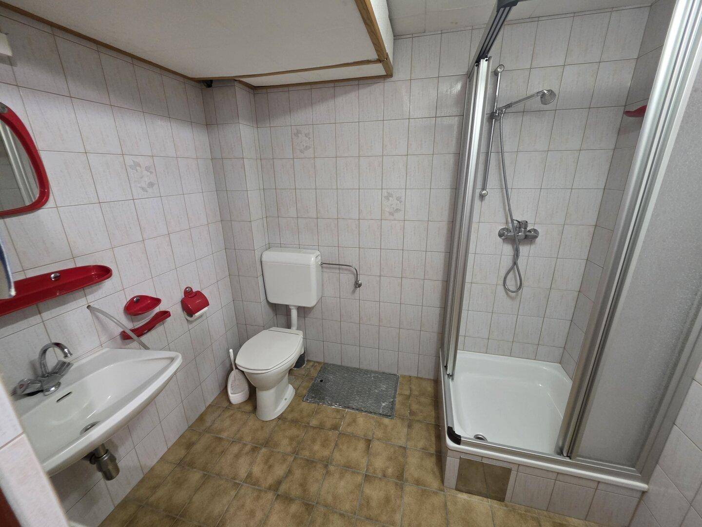Einfaches Badezimmer im Keller mit Dusche, WC und Fliesen an Wänden und Boden.