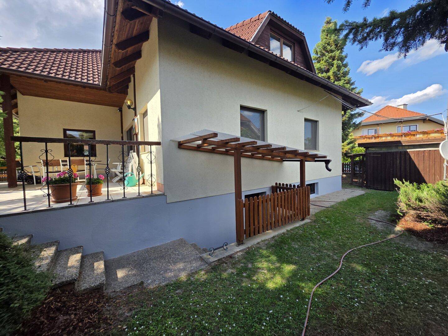 Seitenansicht des Hauses mit überdachtem Bereich, Treppe und gepflegtem Garten.