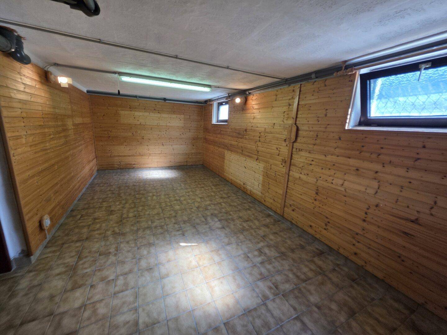Kellerraum mit Holzvertäfelung an den Wänden, Fliesenboden und kleinen Fenstern.