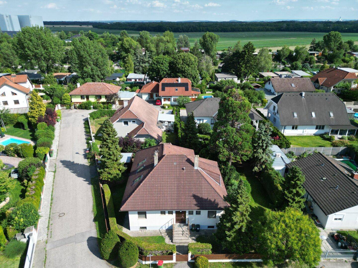 Luftaufnahme einer Wohnsiedlung mit Einfamilienhäusern, viel Grün und einer Straße.