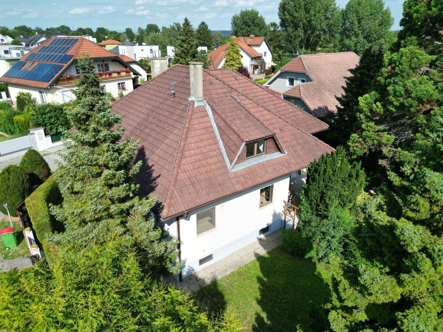 Luftaufnahme eines Einfamilienhauses mit Ziegeldach, umgeben von Bäumen und Sträuchern.