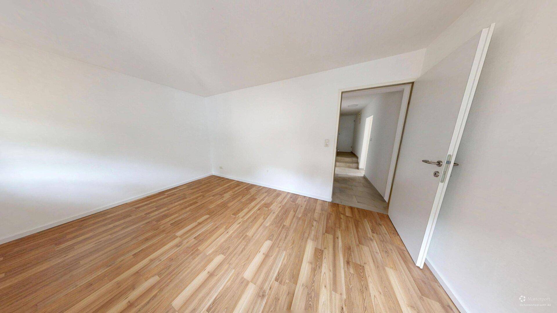 Helles Zimmer mit Laminatboden und offener Tür zu einem Flur, vielseitig nutzbar.