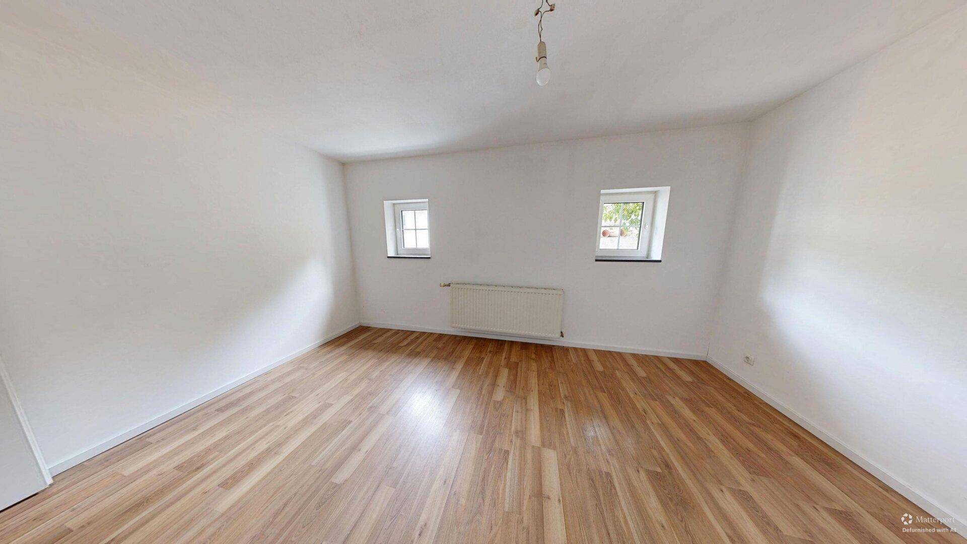 Geräumiges Zimmer mit Laminatboden und zwei Fenstern, die viel Tageslicht hereinlassen.