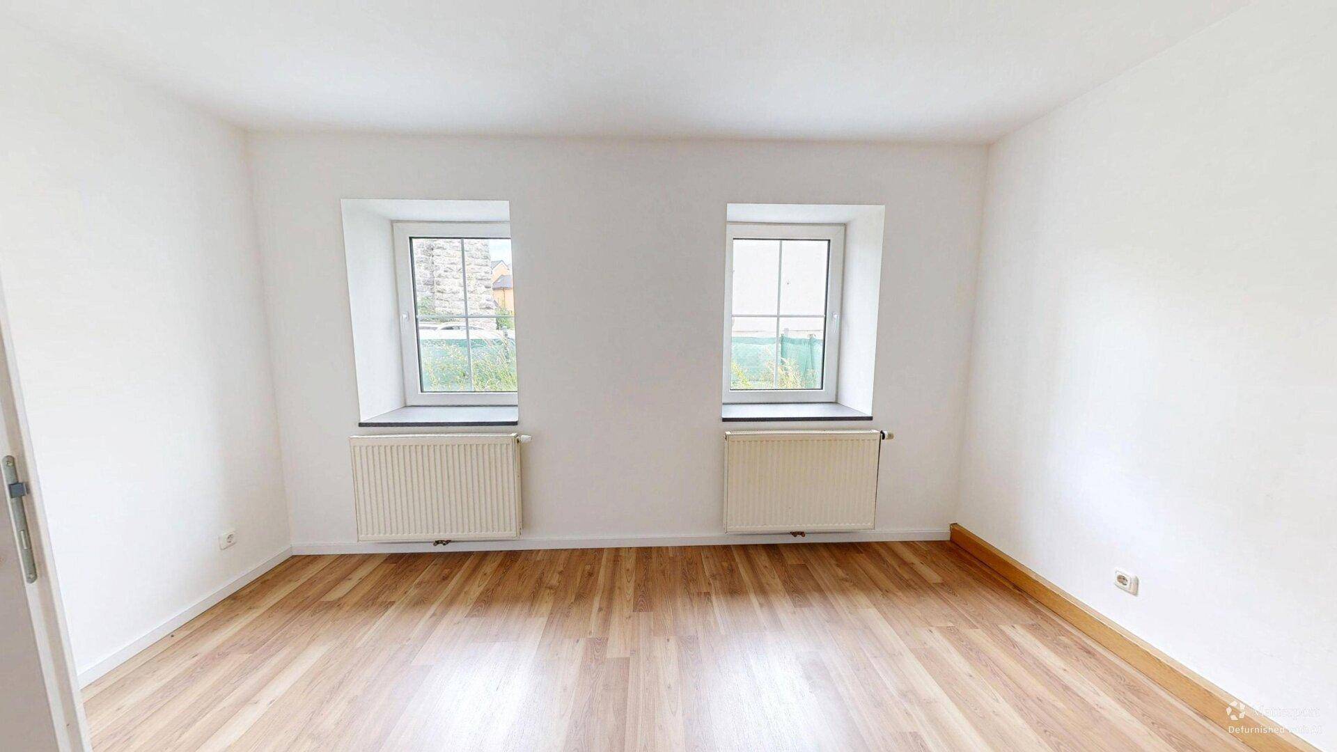 Ruhiges Schlafzimmer mit Laminatboden und zwei Fenstern, ideal für erholsame Nächte.