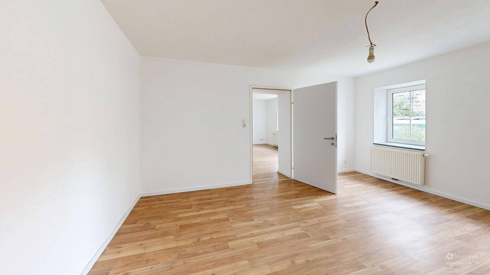 Helles, leeres Zimmer mit Laminatboden und zwei Fenstern, bereit zur individuellen Gestaltung.