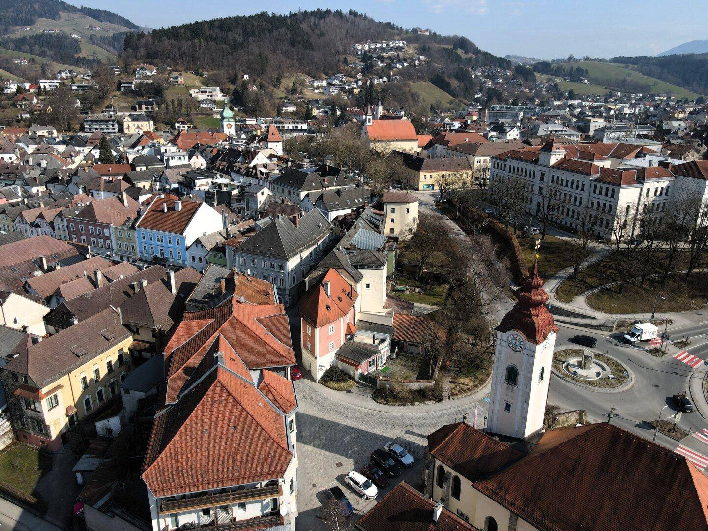 Malerische Luftaufnahme einer Stadt mit historischen Gebäuden, Kirchturm und umliegenden Hügeln.
