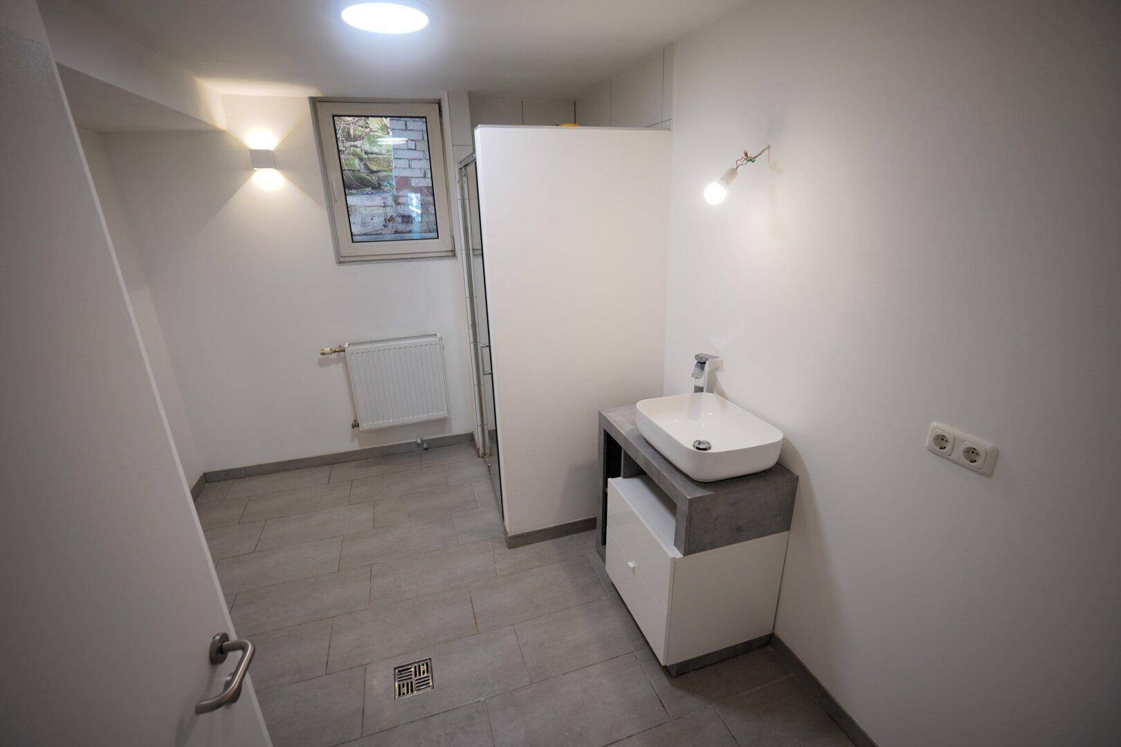 Helles Badezimmer mit Fenster, Duschbereich und modernem Waschbecken auf Waschtisch.