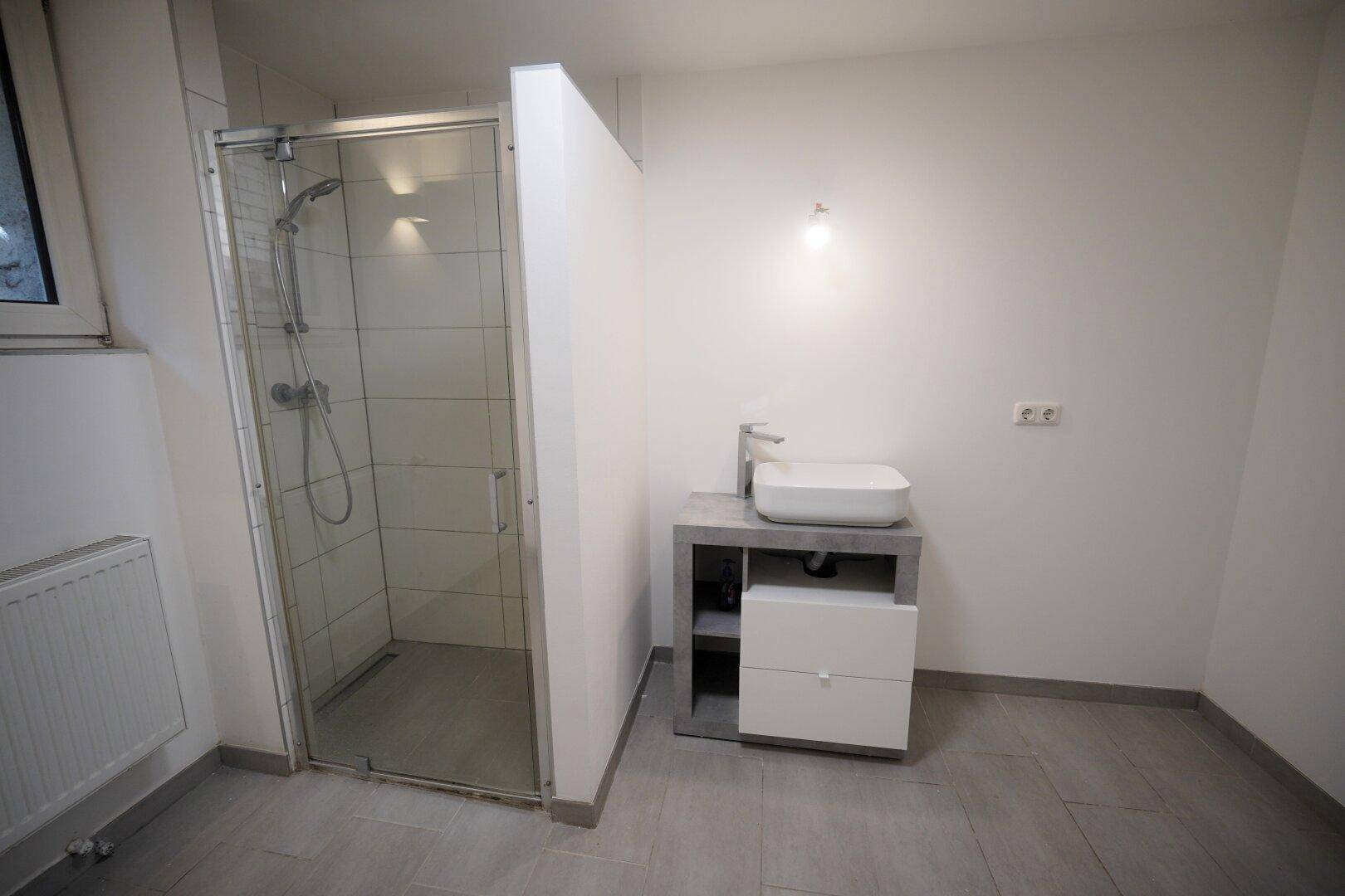 Modernes Badezimmer mit Duschkabine, Waschbecken und grauen Fliesen.