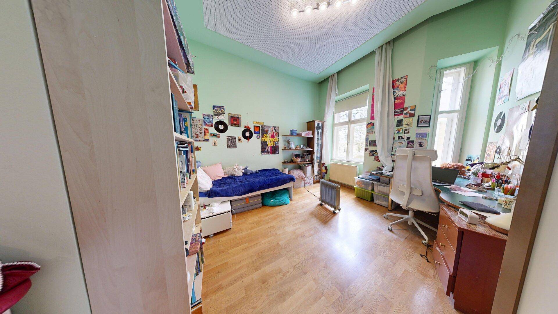 Helles Jugendzimmer mit Einzelbett, Schreibtisch, Bücherregalen und kreativer Wanddekoration.