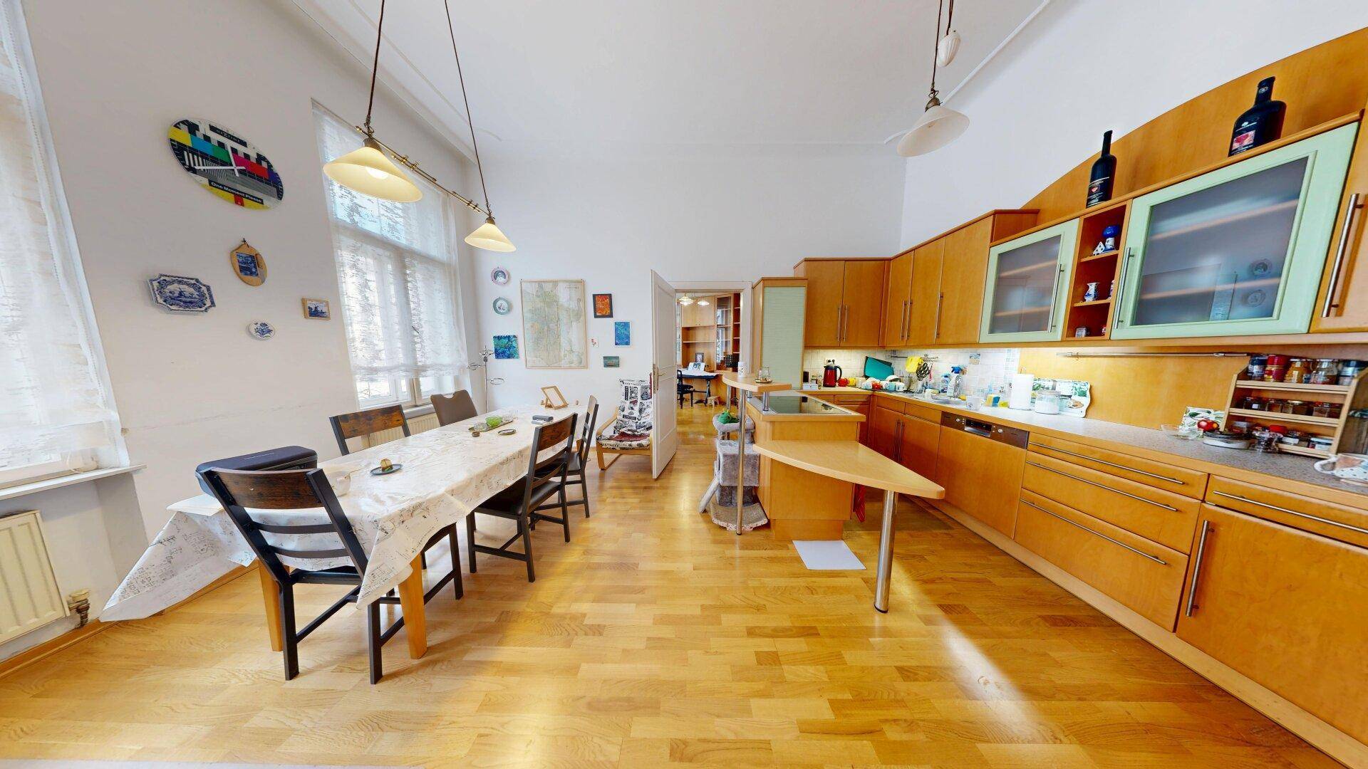 Geräumige Wohnküche mit Holzeinbauten, großem Esstisch und viel Tageslicht durch hohe Fenster.