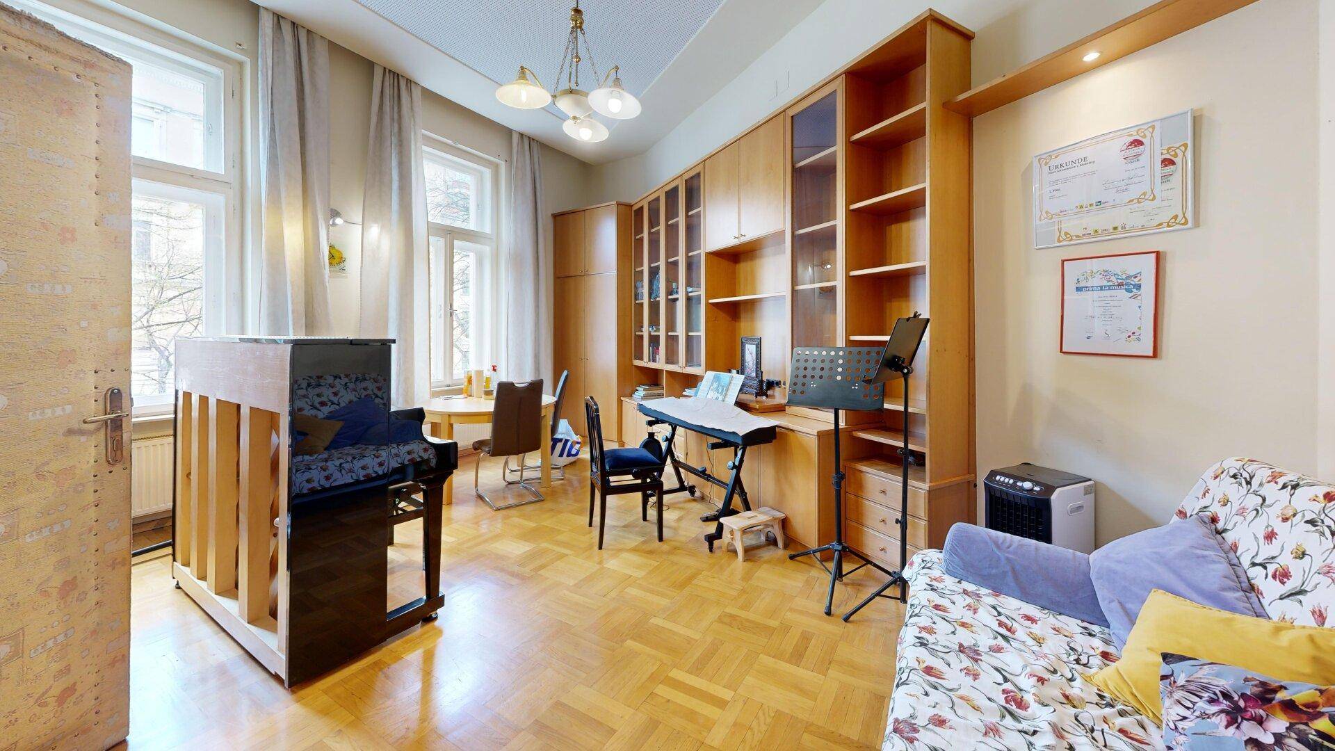 Helles Wohnzimmer mit Flügel, Bücherregalen und gemütlichem Sofa, durchflutet von Tageslicht.