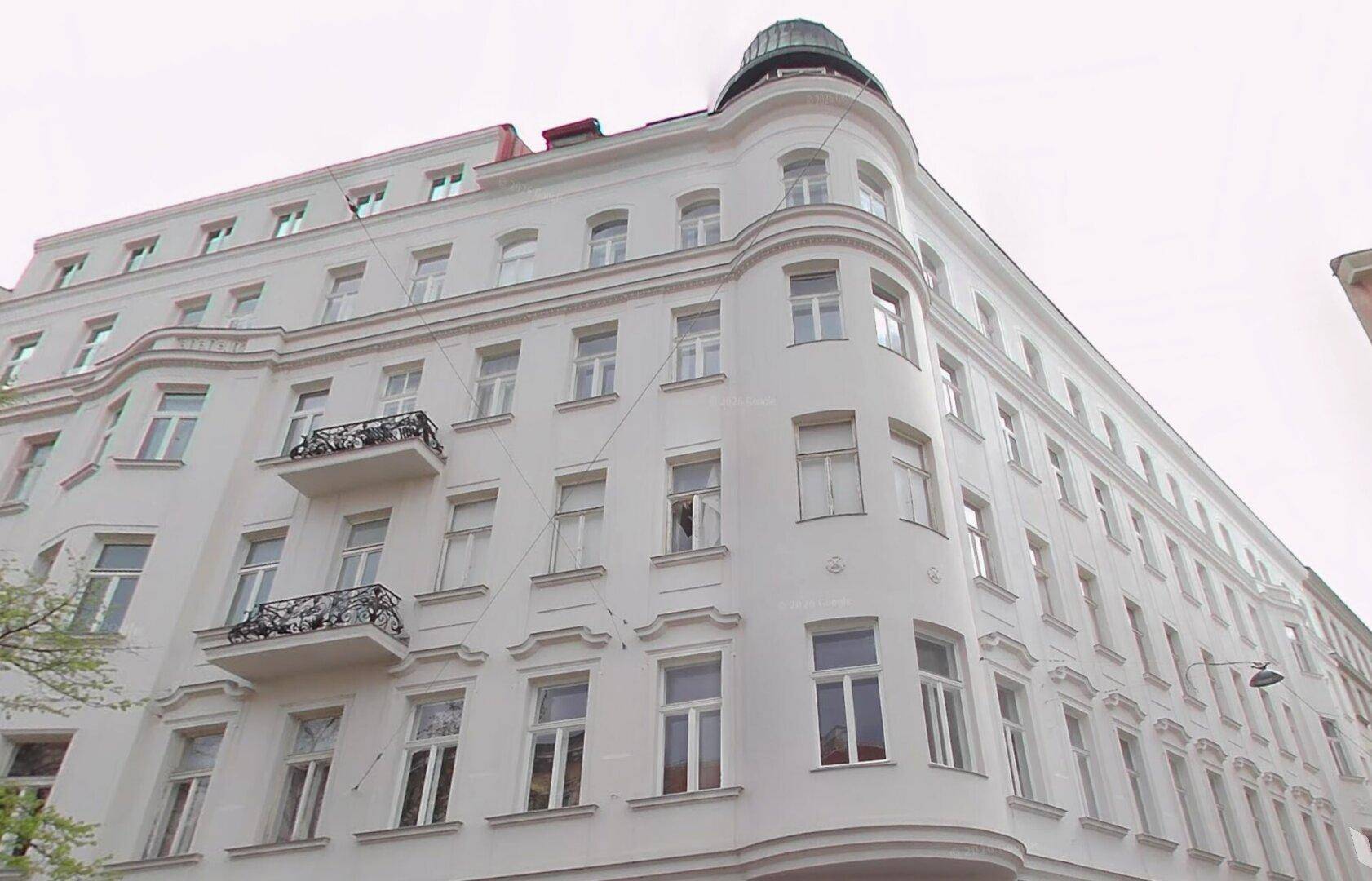 Klassisches Eckgebäude mit weißer Fassade, vielen Fenstern und dekorativen Balkonen.