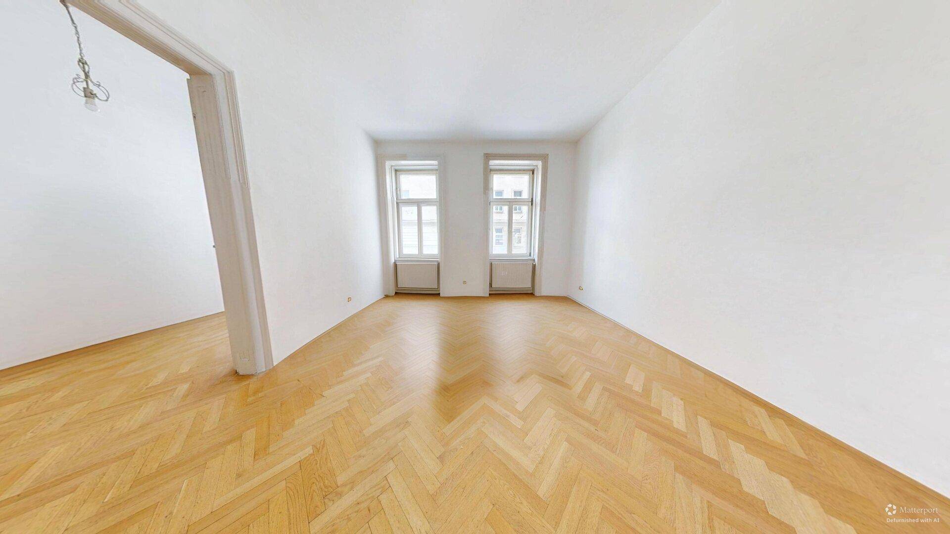 Großes, leeres Zimmer mit Fischgrätparkett und zwei Fenstern, bereit zur individuellen Gestaltung.