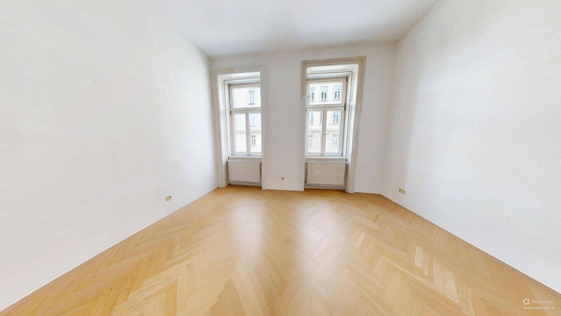 Geräumiges, helles Zimmer mit Fischgrätparkett und zwei hohen Fenstern, vielseitig nutzbar.