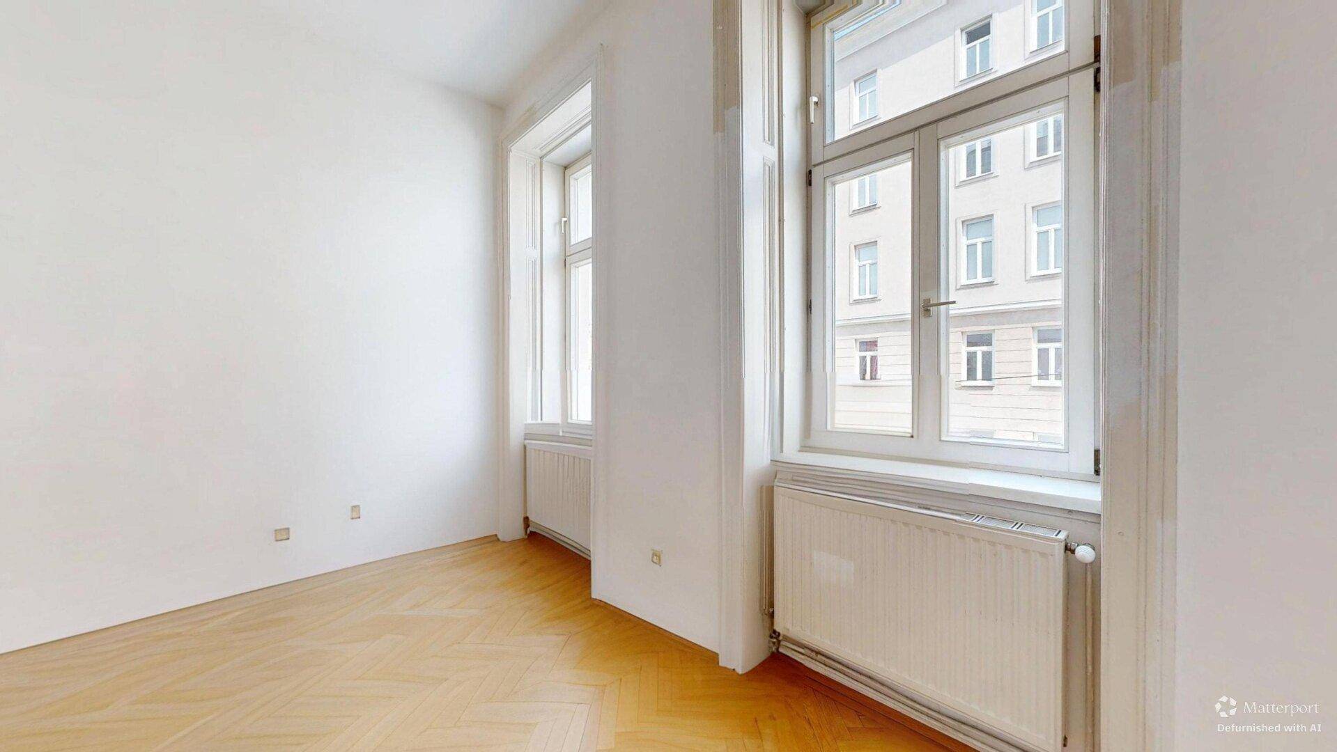 Lichtdurchflutetes Zimmer mit Fischgrätparkett und hohen Fenstern, bietet viel Tageslicht.